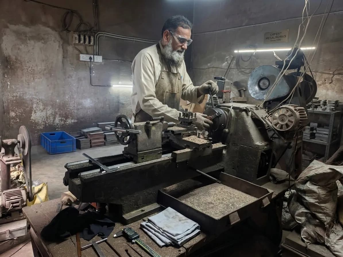 Machinist turning brass components on a lathe at the Nexus Fittings factory in Aligarh, India